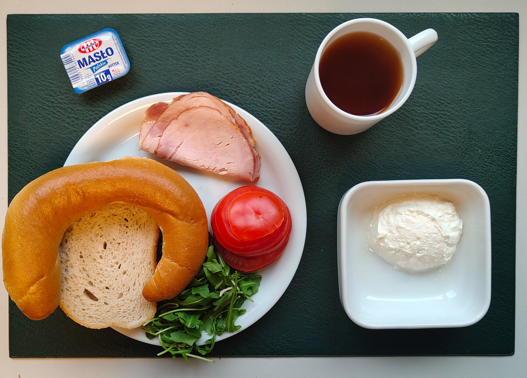 Rogal drożdżowy 50g 1 szt ( GLU PSZ, MLE, GLU ŻYT, ) Chleb mieszany pszenno-żytni 50 g ( GLU PSZ, GLU ŻYT, ) Masło porcjowane 10g (82% tł.) 1 szt ( MLE,) Szynka Wiejska wędzona, wieprzowa, wędzona, pieczona 50 g ( może zawierać: GLU PSZ, SOJ, MLE, SEL, GOR, S02, ) Twarożek domowy waniliowy + 50 g ( MLE, może zawierać: GLU PSZ, JAJ, OZI, SOJ, MLE, ORZ, SEZ,) Plastry pomidora + 110 g Rukola 10 g Herbata czarna ekspresowa z cytryną Cateringowa b/c 250 ml Cukier 5 g