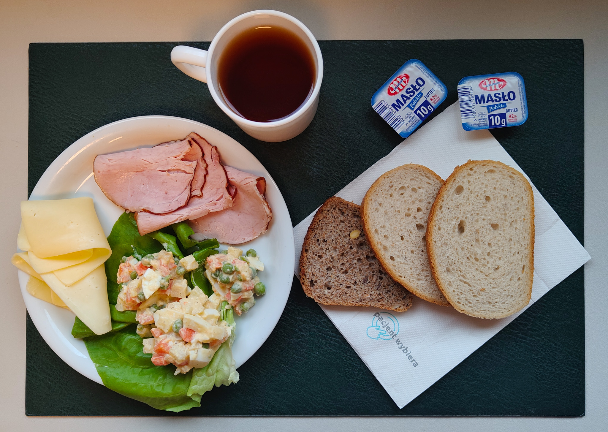 Chleb mieszany pszenno-żytni 50 g ( GLU PSZ, GLU ŻYT, ) Chleb wieloziarnisty 30 g ( GLU PSZ, SOJ, SEZ, GLU ŻYT, ) Masło porcjowane 10g (82% tł.) 2 szt ( MLE,) Ser żółty 30 g (MLE,) Schab Kruchy z Liszek- wieprzowy, parzony, wędzony 50 g ( SOJ, może zawierać: GLU PSZ, MLE, SEL, GOR, S02, ) Sałatka jarzynowa z jajkiem + 120 g ( JAJ, MLE, SEL, GOR, ) Sałata zielona 10 g Herbata czarna ekspresowa z cytryną Cateringowa b/c 250 ml Cukier 5 g