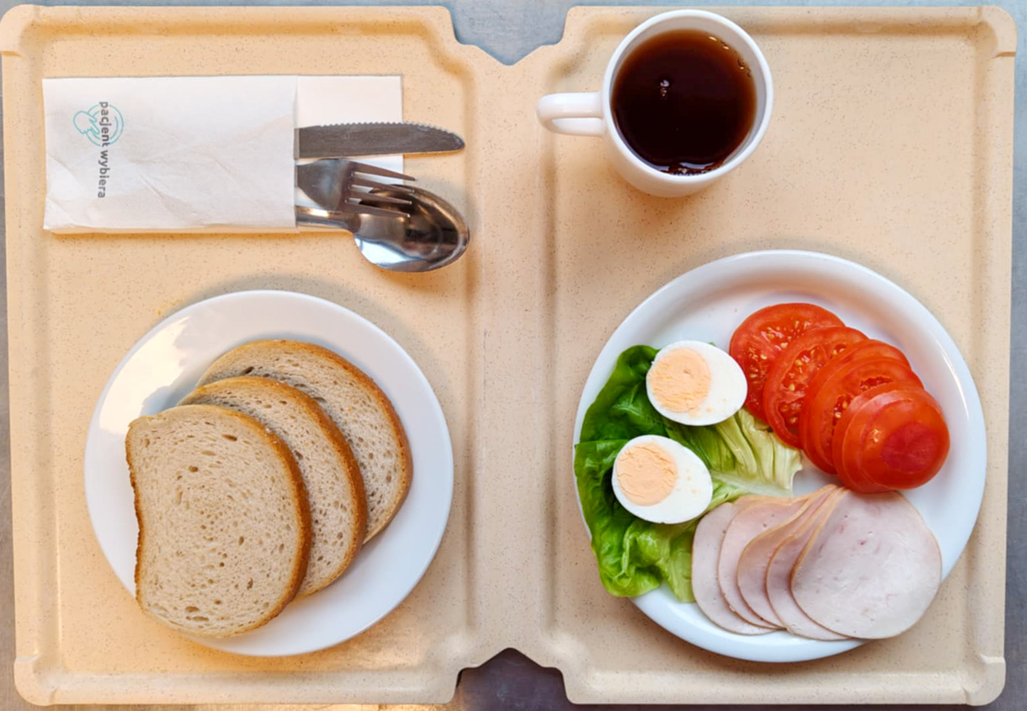 Chleb mieszany pszenno-żytni 80 g ( GLU PSZ, GLU ŻYT, ) Masło porcjowane 10g (82% tł.) 1 szt ( MLE,) Jajko gotowane kl M + 1 szt ( JAJ,) Szynkowa dębowa drobiowa kiełbasa grubo rozdrobniona 50 g Plastry pomidora + 100 g Sałata zielona 20 g Herbata czarna ekspresowa z cytryną Cateringowa b/c 250 ml Cukier 5 g