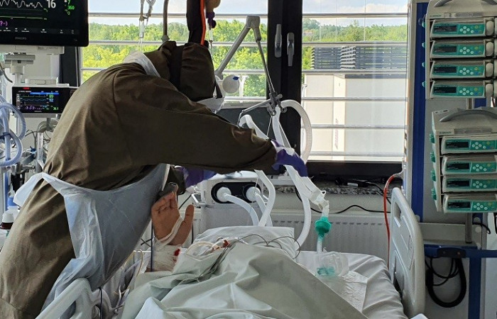 Oddział covid - pracownik w kombinezonie ochronnym pochyla się nad łóżkiem pacjenta 