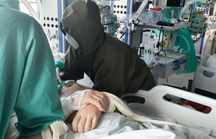 Oddział covid - pracownik w kombinezonie ochronnym pochyla się nad łóżkiem pacjenta 