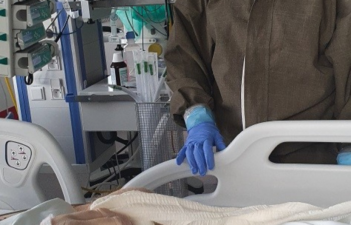 Oddział covid - pracownik w kombinezonie ochronnym pochyla się nad łóżkiem pacjenta 