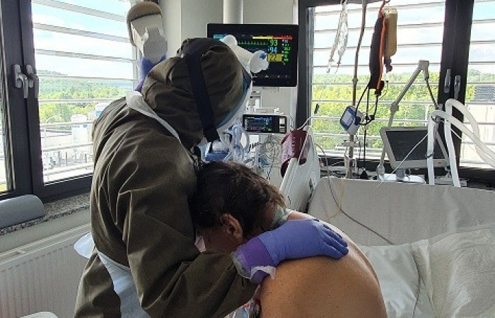 Oddział covid - pracownik w kombinezonie ochronnym pochyla się nad łóżkiem pacjenta 