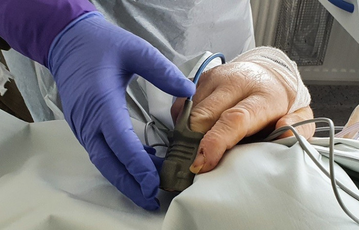 Oddział covid - pracownik w kombinezonie ochronnym pochyla się nad łóżkiem pacjenta 